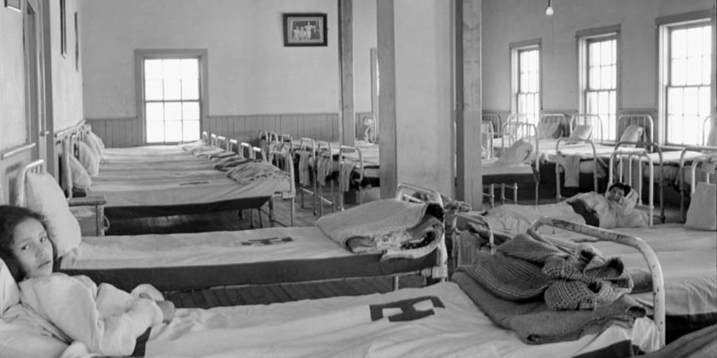 Two Cree girls in their beds in the girls' dormitory at All Saints Indian Residential School, Lac La Ronge, Saskatchewan, March 1945