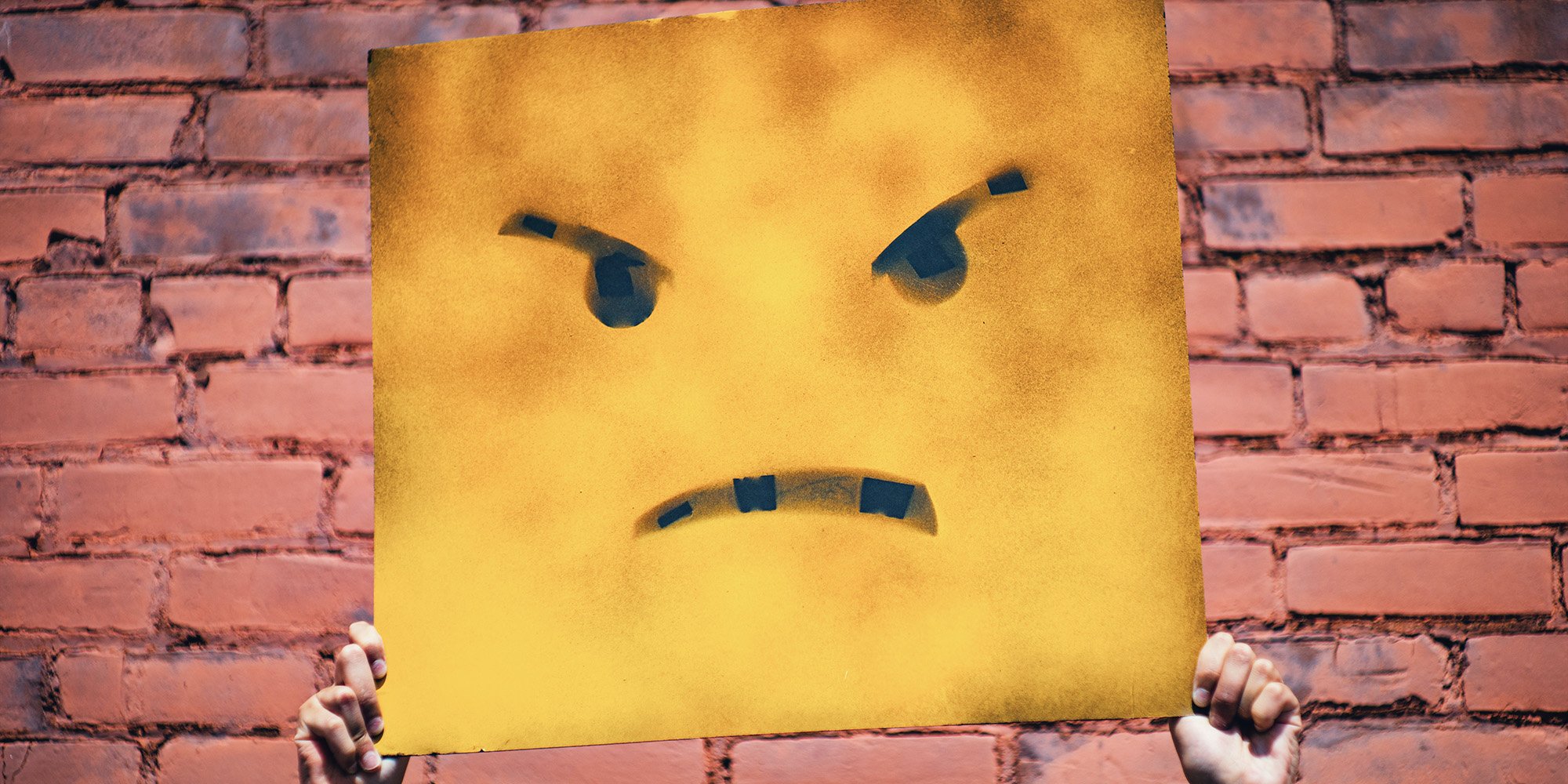 angry face on a sign being held up by hands
