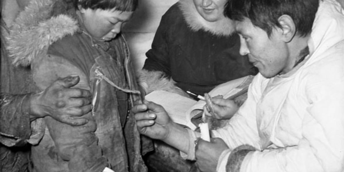 Inuit boy and man checking Eskimo tag for census, Windy River, Nunavut, 1950. Photo: LAC a102695-v6