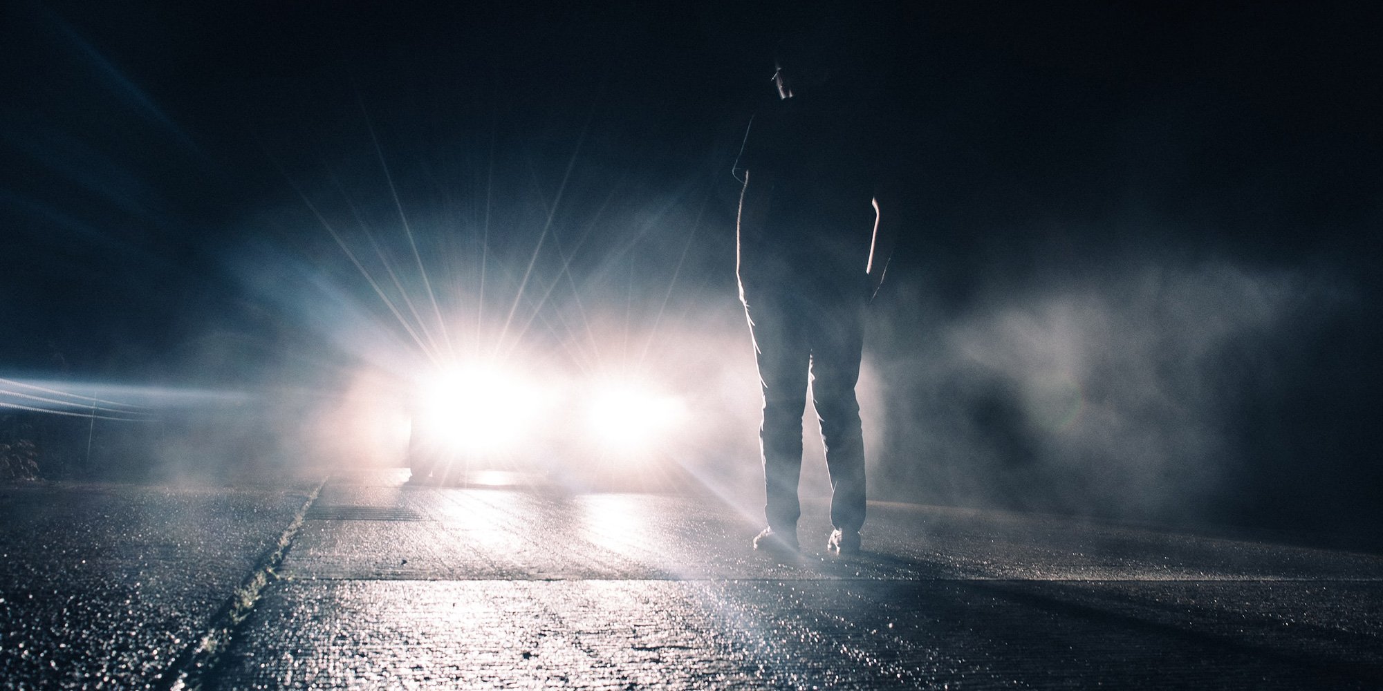 man standing in front of car headlights