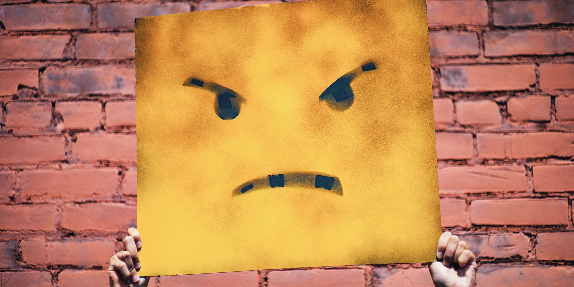 angry face on a sign being held up by hands